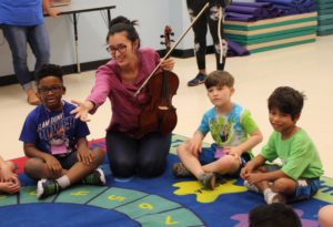 Woman with viola leads a musical activity for children at a summer camp.