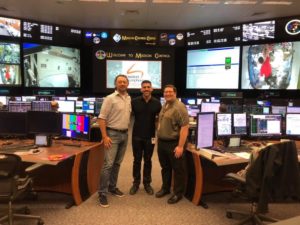 Three men pose for a photo in NASA's Mission Control Center.