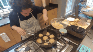 Woman frying potato latkes in oil on a stove.