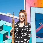 Jess Gillam holding a soprano saxophone in front of a colorful backdrop